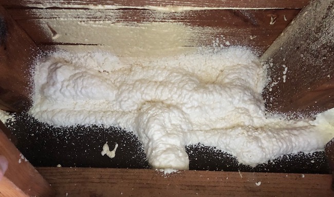 Spray foam from a two-part foam kit sealing and insulating the sheathing and the top plate