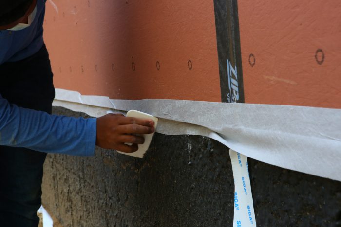 Air-sealing tape lapping liquid-applied waterproofing at foundation